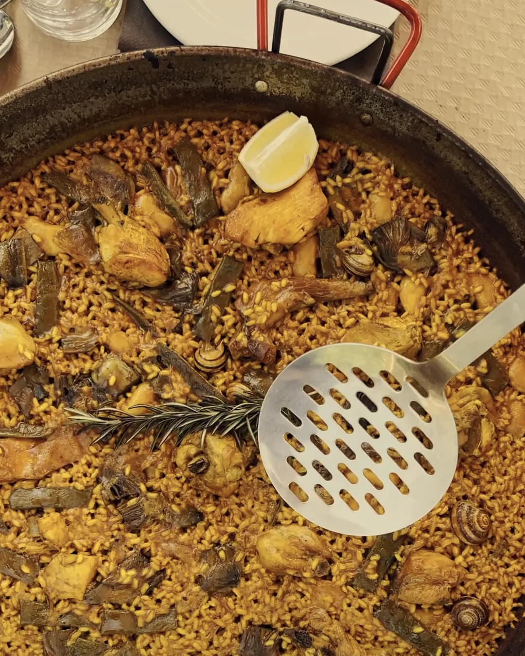 A Valencian paella seen from above, with the serving spoon and a wedge of lemon