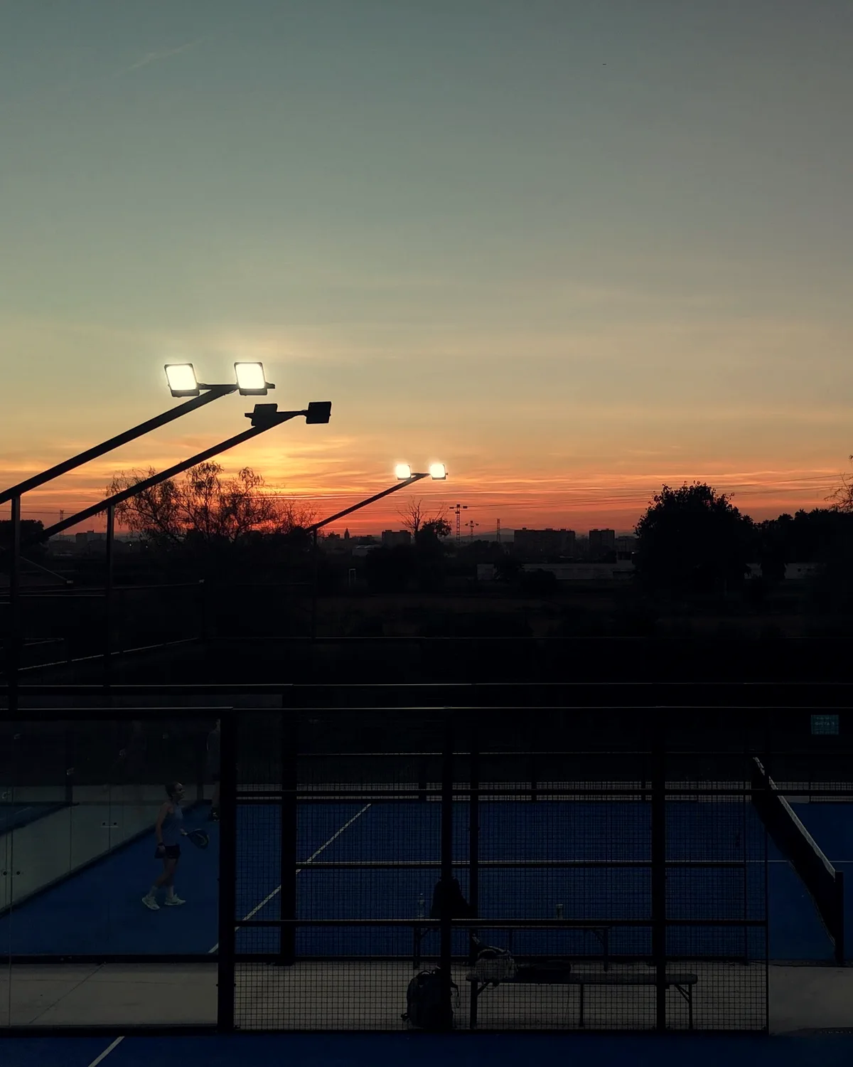 Padel courts at dusk with the floodlights on, seen from a drone