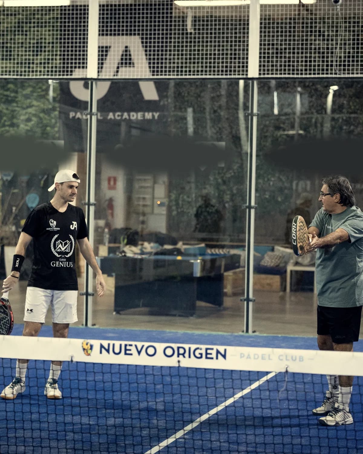 A coach shows a player the racket movement by the net on an indoor court