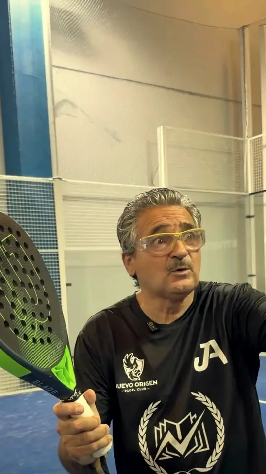 A JA coach explains a shot, racket in hand, on an indoor court.