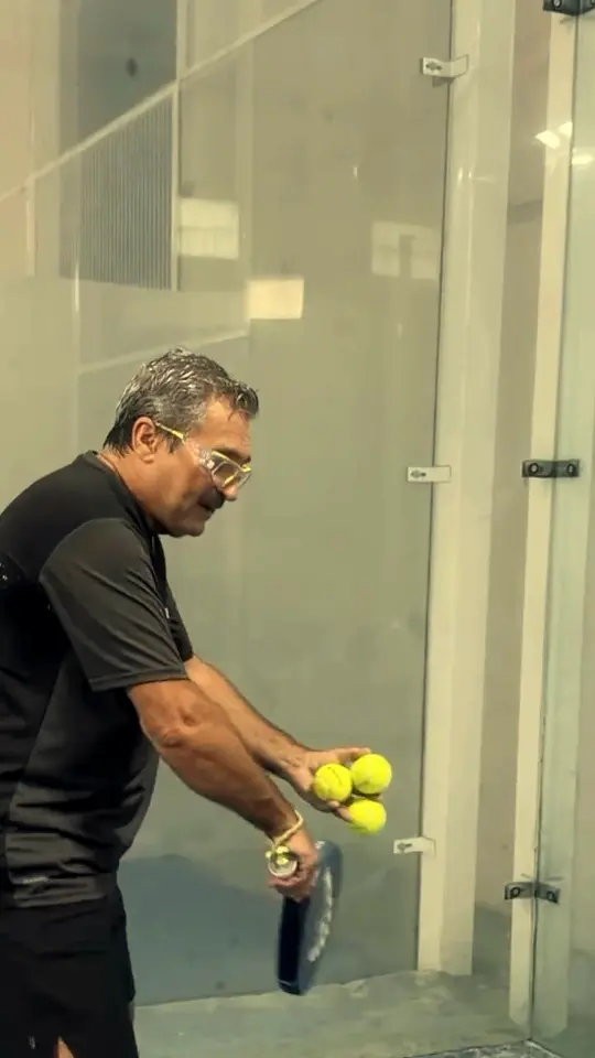 A JA coach holding a racket and a ball on a blue indoor court.