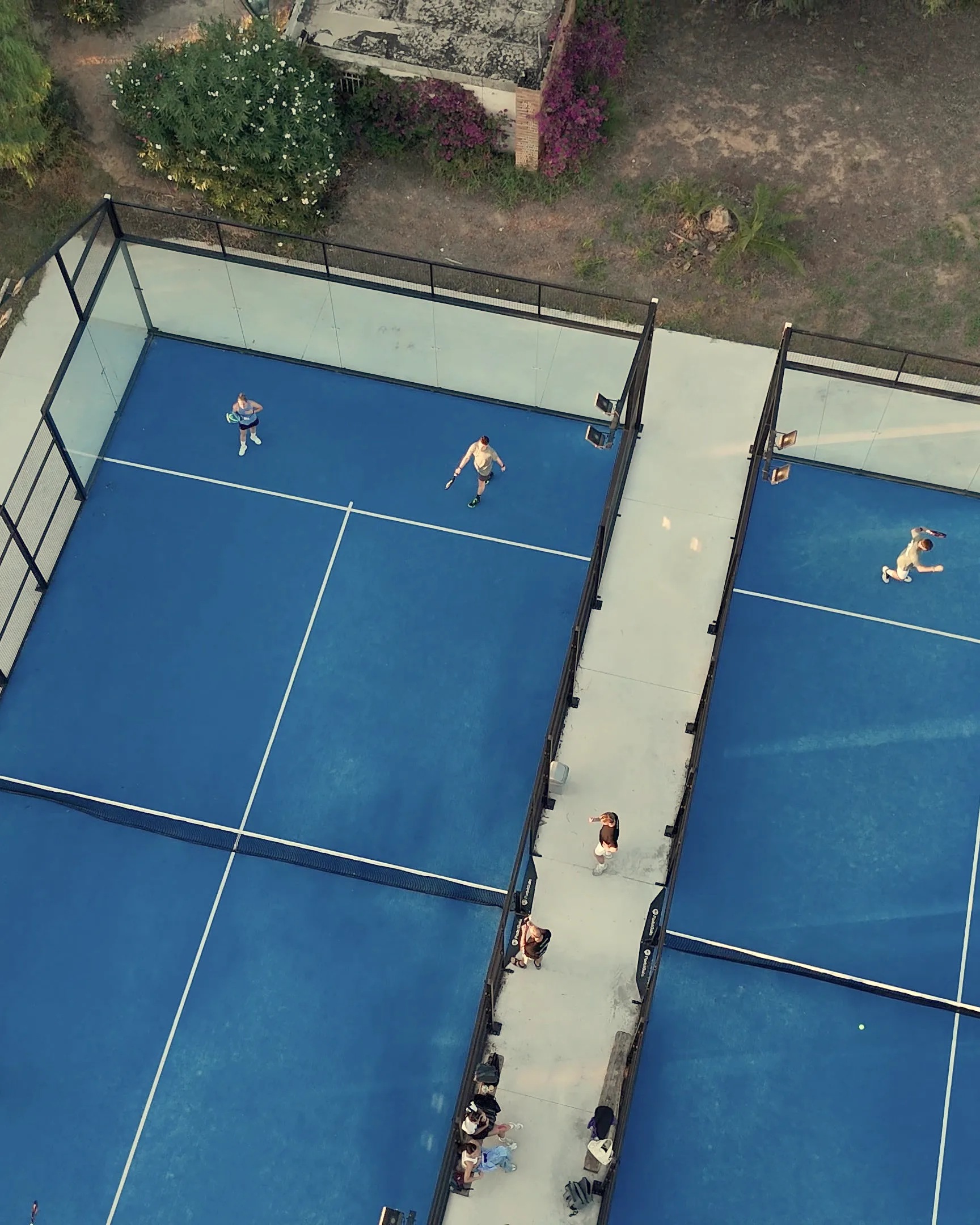 Two courts at Club Deportivo Saladar seen from a drone, with the walkway between them and the trees around